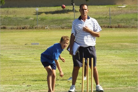 Leon Wessels van Laerskool Gansbaai boul terwyl die afrigter van Die Bron, Graham Stieger toekyk.